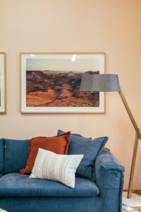 Interior of light living room decorated with soft couch with pillows near floor lamp and paintings hanging on wall